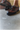 A close-up of a person walking on a concrete floor wearing polished brown leather dress shoes with decorative perforations. One shoe is in focus while the other is slightly blurred in motion, highlighting the dynamic action.