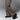 A person stands on a gray background, showing only the lower half of their legs in loose, light brown pants and Anthony Veer Harbor Moc Sandal // Obsidian Oil Black crafted from premium Italian cowhide leather with rugged detailing.