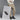 A person in a cream sweater and beige pants stands by a large Anthony Veer ad for the Harbor Moc Sandal // Chestnut Grain Brown, crafted from Italian cowhide leather. They wear similar shoes and have their arms crossed.