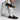An individual in white pants and socks is seated, featuring the Anthony Veer Dunhill Single Monk shoes in Tobacco Velvet Brown Suede. These Italian cowhide loafers have a sleek design with buckle detail, showcasing Bologna construction against a minimalist background.