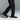 The image captures a person in black dress pants and Anthony Veers Belmont Penny Loafers in Onyx Shine Black, crafted from Italian leather, mid-step against a gray background, highlighting the sleek footwear and formal attire.